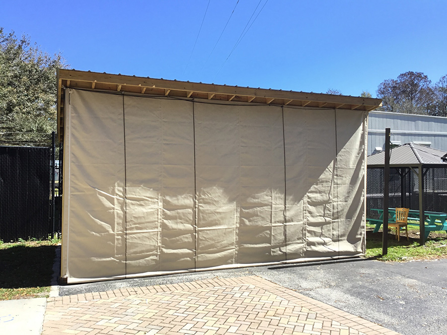 Beige heavy-duty industrial curtain installed on a wooden-framed outdoor structure, providing durable weather protection in a commercial setting.