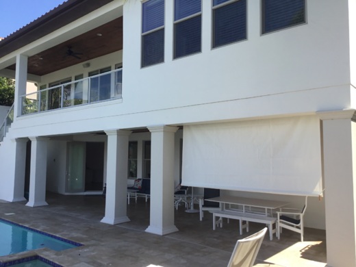 White heavy-duty outdoor curtain providing shade and privacy for a residential patio area near a pool, supported by elegant columns.
