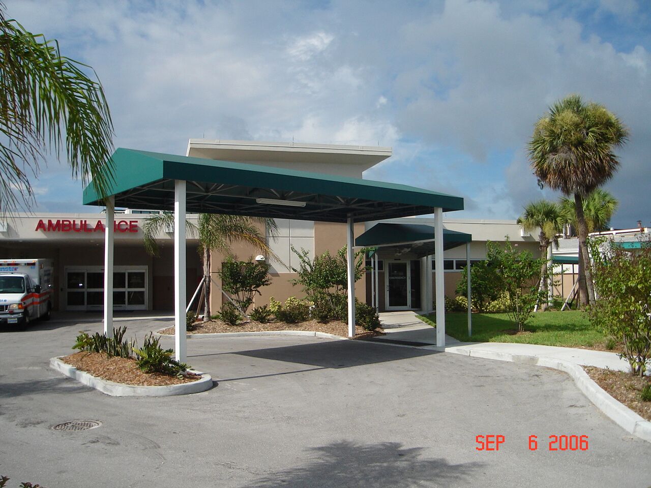 Green fabric awning with white metal supports providing shade at a hospital ambulance entrance, blending functionality with durability.