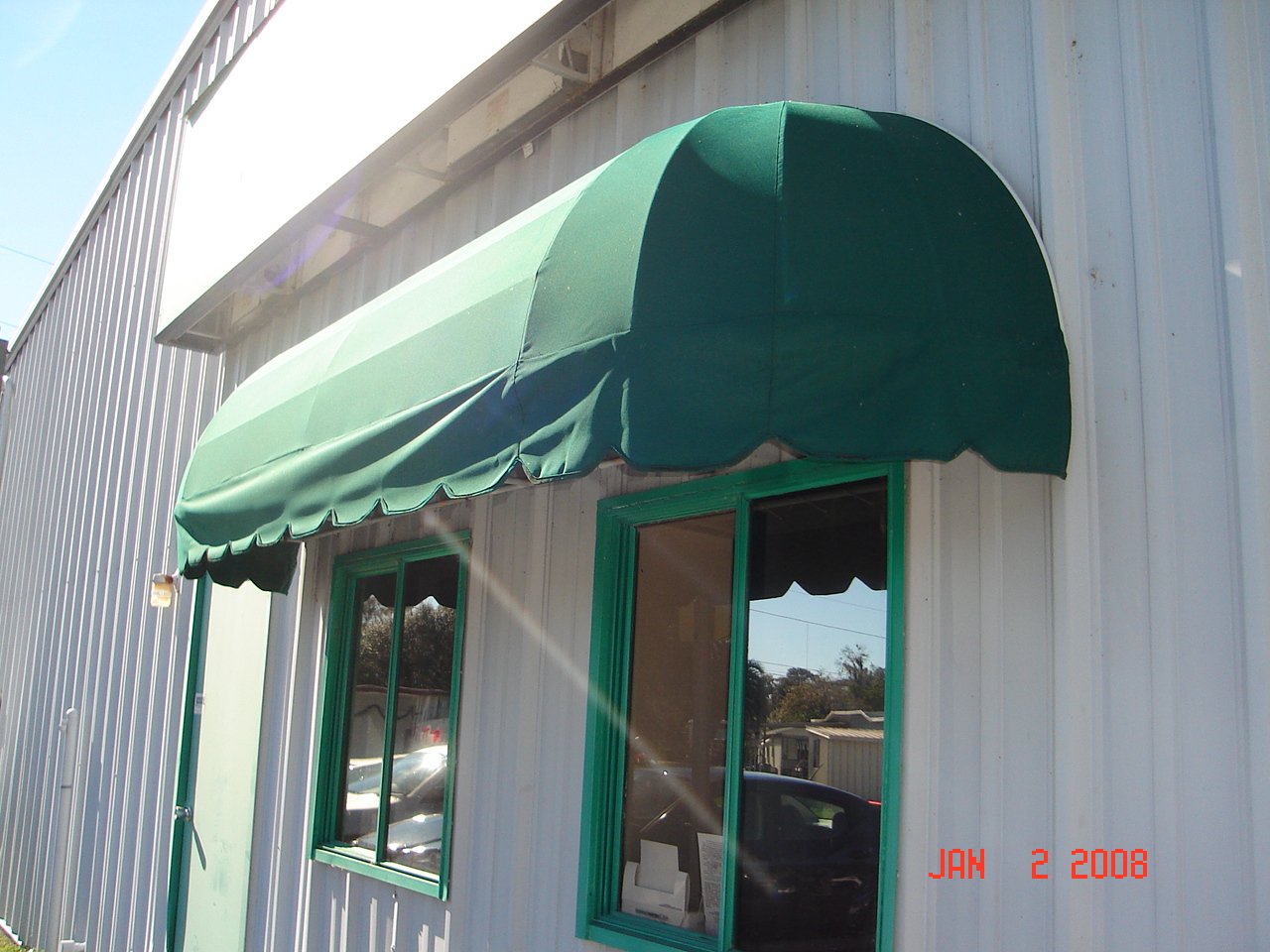 Green canvas awning with scalloped edges installed over a commercial building window, providing shade and weather protection.