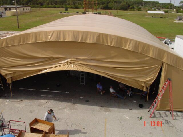 Tan heavy-duty industrial curtain enclosing a large outdoor structure, providing durable weather protection for a commercial setting.